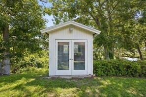 A small, white wooden structure with a gabled roof and two glass doors, surrounded by lush greenery. - Waterfront Amelia Island home with amazing views, deck, parking. (Fernandina Beach)