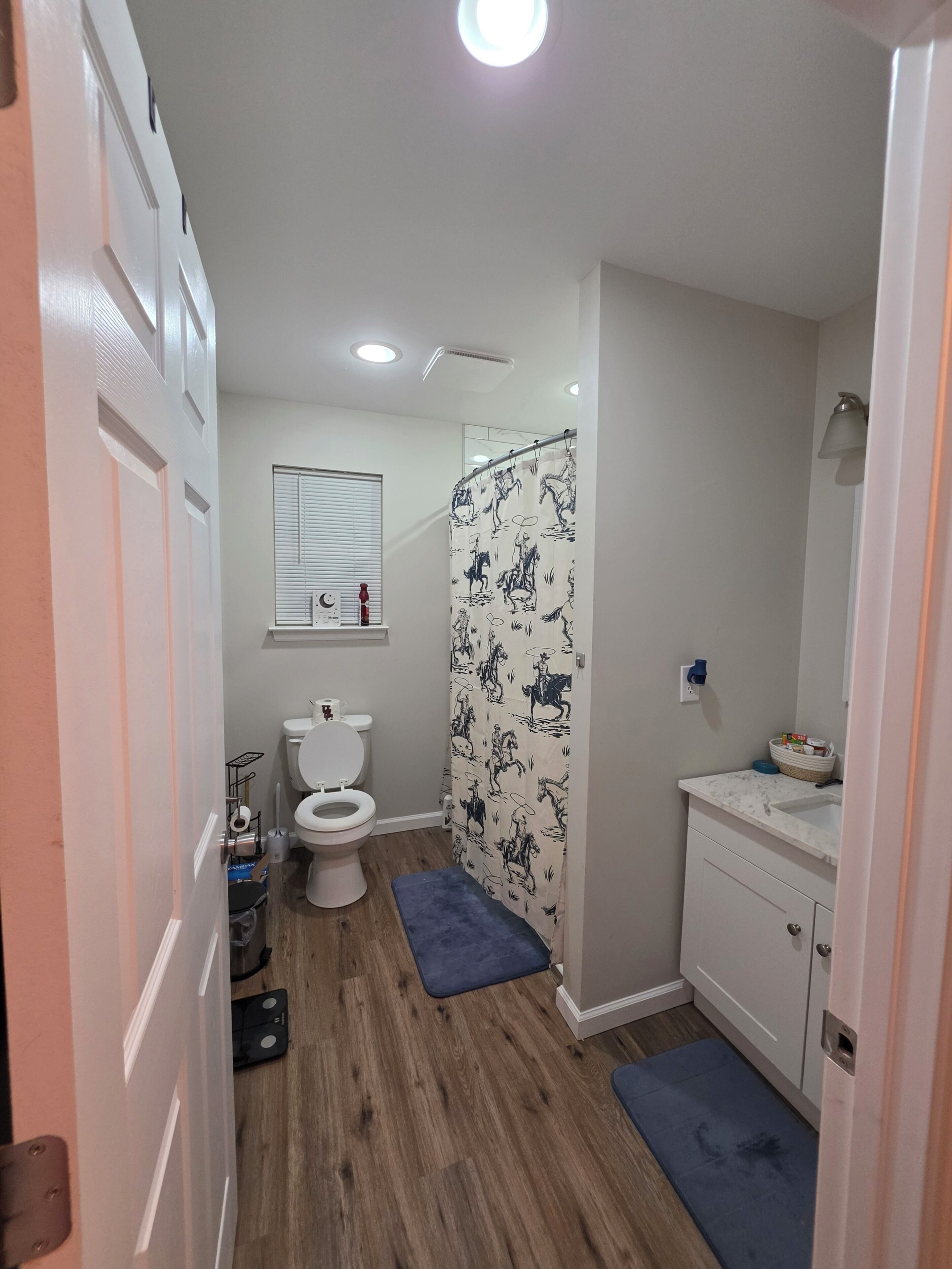 Baño con inodoro, cortina de ducha, lavabo y piso de madera.
