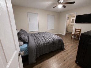 Ein Schlafzimmer mit einem Bett, einem Deckenventilator und Blick zur Küche.