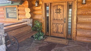 Entrada de una cabaña de madera con un felpudo, un banco y un farol.