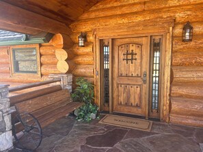 Eingang eines Holzchalets mit Fußmatte, Bank und Laterne.