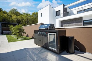 An outdoor kitchen with a grill, oven, and speakers, adjacent to a modern house with a balcony. - Villa Azoria with pool and jacuzzi (Kvarner - Žgaljići) (Žgaljići)