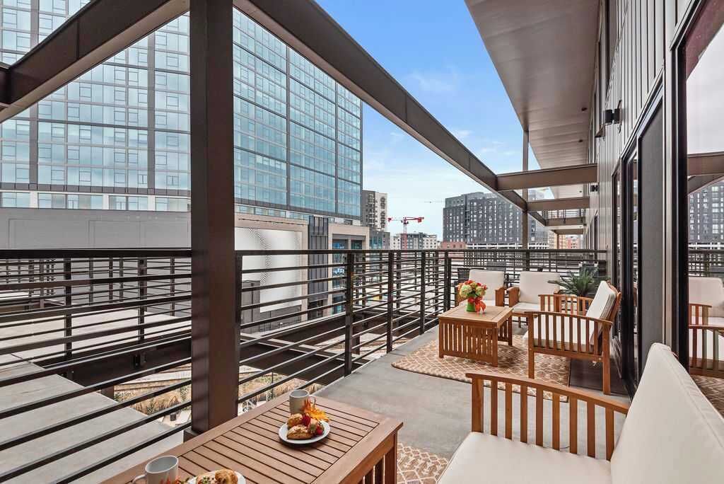 A balcony with a view of a modern building, furnished with a table and chairs, and a railing.