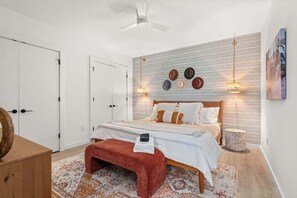 Ein Schlafzimmer mit einem Bett, Nachttischlampen, einem Deckenventilator, einer Wandleuchte und einer Tür.