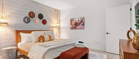 Une chambre à coucher avec un lit, une table de chevet et une étagère murale où sont posés des chapeaux.