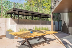 A modern outdoor seating area with a wooden table and benches, a metal pergola, and a concrete wall with greenery. - Penthouse Combo | Pool, Views, Near Broadway (Nashville)