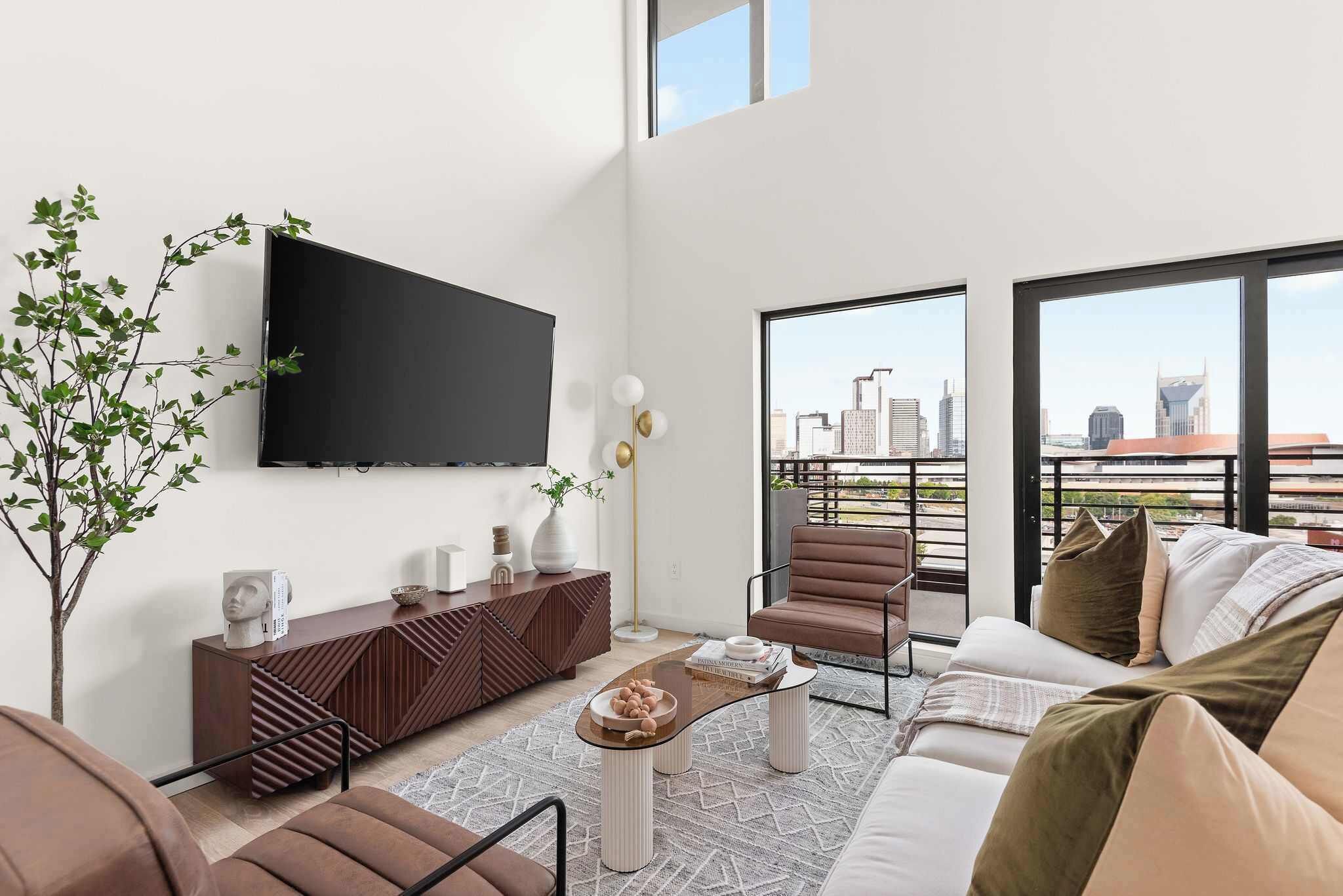 A modern living room with a sofa, armchairs, a coffee table, a TV, and a city view.