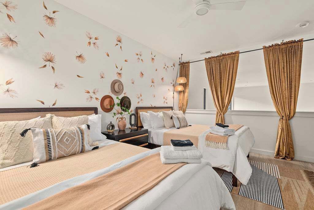 A hotel room with two beds, a nightstand, a lamp, and a window with curtains.