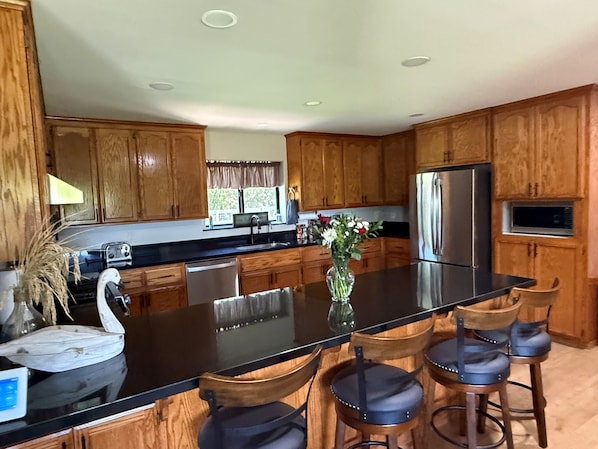 A kitchen with wooden cabinets, a stainless steel refrigerator, a black countertop, and a vase with flowers.