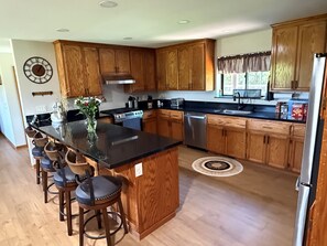Una cocina moderna con armarios de madera, una isla central con taburetes de bar, electrodomésticos de acero inoxidable y un reloj en la pared.