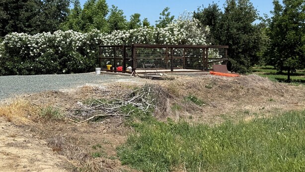 A fenced outdoor area with a gravel path, surrounded by greenery and trees.
