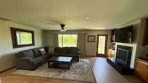 A living room with a sectional sofa, a coffee table, a ceiling fan, and a television.
