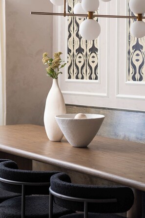 A dining table with a white vase and a bowl, a patterned wall, and a hanging light fixture. - The Grand Skyline | 2 Designer Condos, Pool, Gym (Nashville)