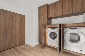 A laundry room with two front-loading washers and wooden cabinets. - The Grand Skyline | 2 Designer Condos, Pool, Gym (Nashville)