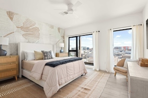 A bedroom with a bed, bedside tables, a desk, a chair, a ceiling fan, and a large window with curtains. - The Grand Skyline | 2 Designer Condos, Pool, Gym (Nashville)