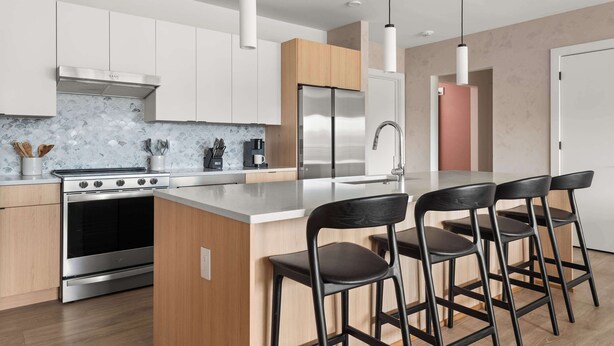 A modern kitchen with a central island, stainless steel appliances, and black bar stools. - The Grand Skyline | 2 Designer Condos, Pool, Gym (Nashville)