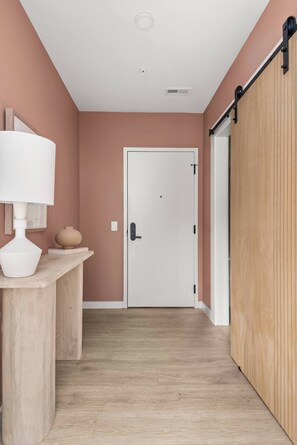 A hallway with a white door, a wooden counter with a white lamp, and a sliding barn-style door. - The Grand Skyline | 2 Designer Condos, Pool, Gym (Nashville)