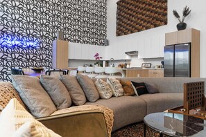 A modern living room with a sofa, a coffee table, and a kitchen in the background. - The Grand Skyline | 2 Designer Condos, Pool, Gym (Nashville)