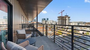 A balcony with wicker furniture, a view of the cityscape, and a construction crane in the distance. - The Grand Skyline | 2 Designer Condos, Pool, Gym (Nashville)