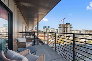 A balcony with wicker furniture, a view of the cityscape, and a construction crane in the distance. - The Grand Skyline | 2 Designer Condos, Pool, Gym (Nashville)