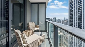 Ein Balkon mit zwei Stühlen und einer Glasreling mit Blick auf eine Stadtlandschaft.