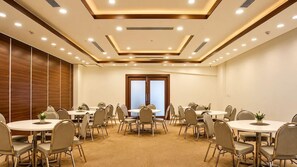 Una sala de conferències amb taules i cadires rodones, un gran finestral i il·luminació encastada al sostre.