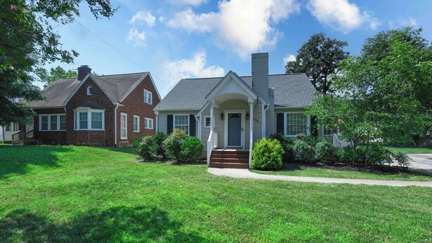 A two-story house with a front porch, a chimney, and a well-maintained lawn. - Prime location near downtown-minutes to Market area, Truist Point, and HPU (High Point)