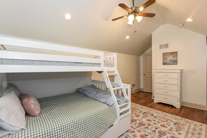 Una cama individual superpuesta con escalera, un ventilador de techo, iluminación empotrada, una puerta y un aparador con cajones.