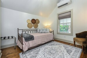 A bedroom with a bed, a bedside table, a chair, a window, and a wall-mounted air conditioner. - Prime location near downtown-minutes to Market area, Truist Point, and HPU (High Point)