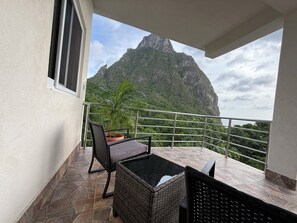 Een balkon met uitzicht op een berg, een potplant en een rieten stoel.
