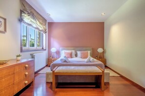 Ein Schlafzimmer mit einem Bett, Nachttischen, einer Kommode, einem Fenster mit Vorhängen und einer Heizung.