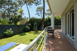 A balcony with a table and chairs, a grassy yard, and a view of trees and a fence. - Casa das Andorinhas by Hommelier (Fão)