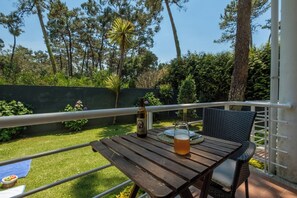 Une table en bois, sur laquelle se trouvent une bouteille et un verre de bière, est placée sur un balcon d’où l’on peut admirer des arbres et un mur végétal.