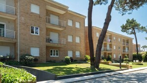 A multi-story residential building with balconies, a paved courtyard, and surrounding greenery.
