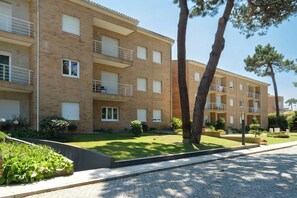 A multi-story residential building with balconies, a paved courtyard, and surrounding greenery.