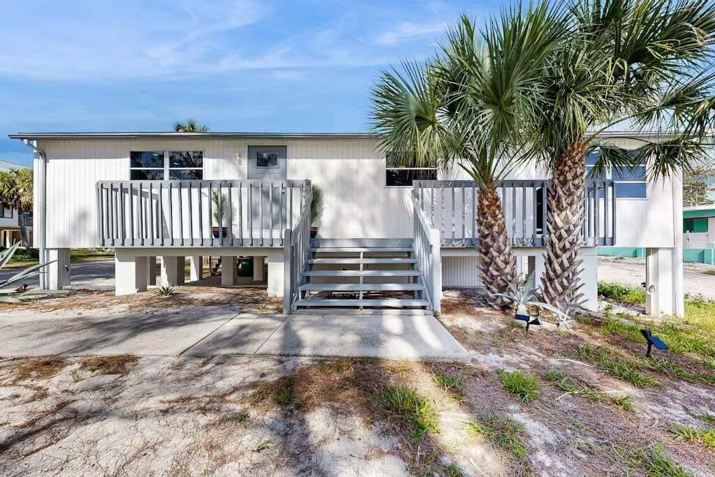 A two-story building with a front porch, palm trees, and a concrete driveway.