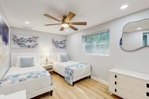 Ein Schlafzimmer mit zwei Betten, einem Deckenventilator, einem Nachttisch mit Lampe, einer Kommode und Bildern an den Wänden.