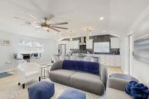 A modern living room with a sofa, ottomans, and a dining area with chairs. - Newly Renovated Beach Retreat Just Steps from Englewood Beach - Beach Barracks - Roelens (Englewood)