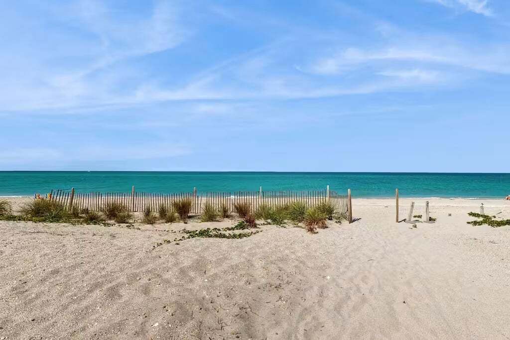 A sandy beach with a wooden fence and sparse vegetation.