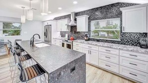 Una cocina moderna con una isla grande, muebles blancos y un salpicadero blanco y negro.