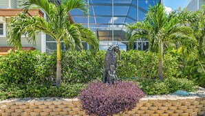 Eine angelegte Grünfläche mit einer Statue, Palmen und einem modernen Gebäude im Hintergrund.