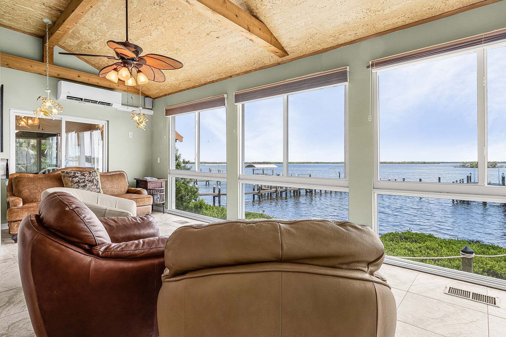 A spacious room with a large window overlooking a body of water, a ceiling fan, and a leather sofa.