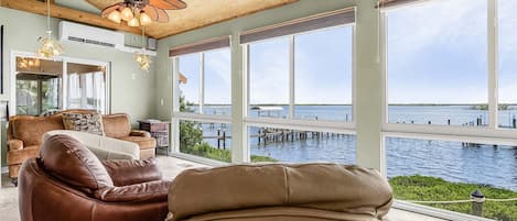 A spacious room with a large window overlooking a body of water, a ceiling fan, and a leather sofa.