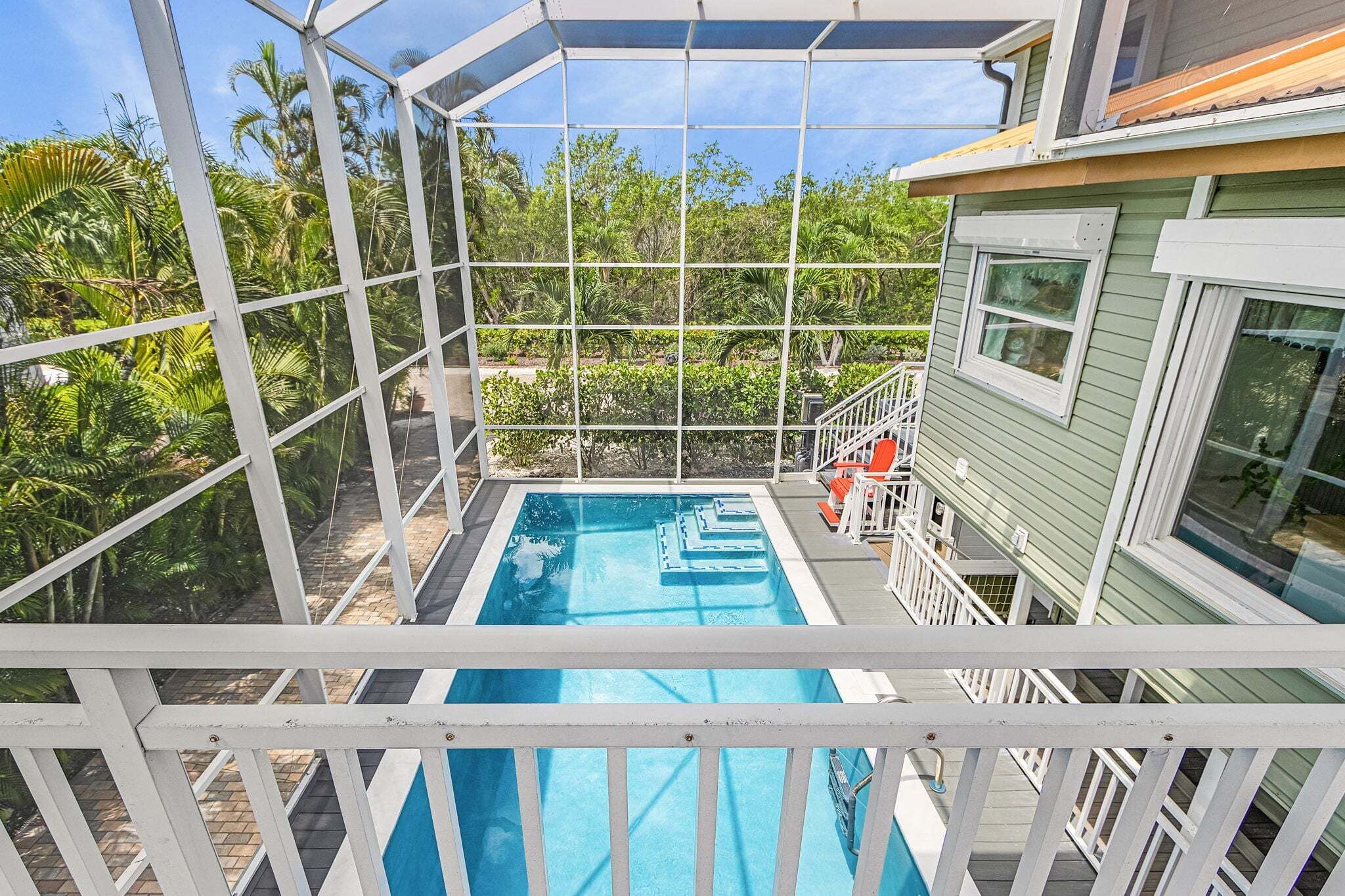 A pool with a white deck and a glass enclosure, surrounded by lush greenery.