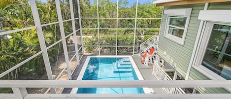 Piscina con cubierta blanca y cerramiento de vidrio, rodeada de exuberante vegetación.