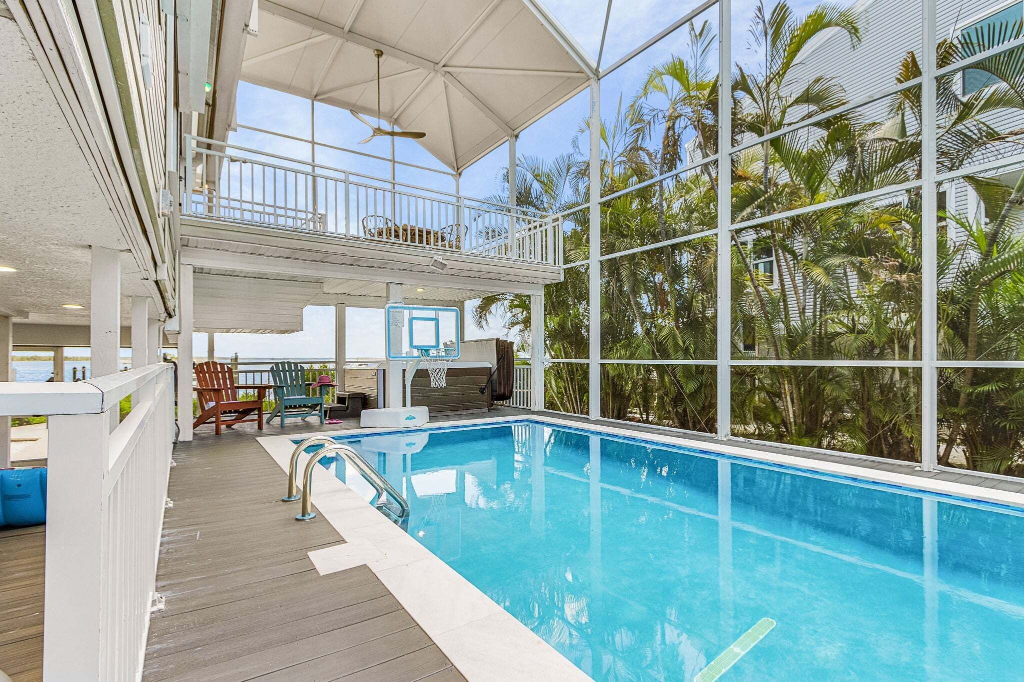 Zona de piscina con canasta de baloncesto, mobiliario exterior y vista a palmeras.