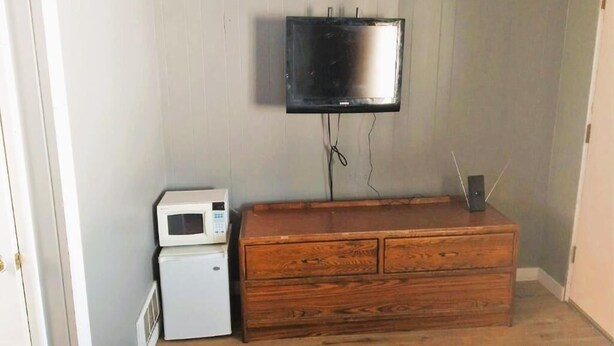 A room with a television mounted on the wall, a microwave, and a wooden dresser. - Desert Inn and RV (Shoshoni)