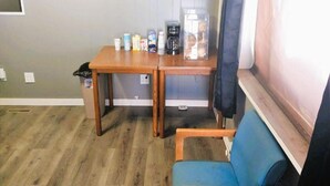 A small room with a wooden table, a blue chair, and a window with curtains. - Desert Inn and RV (Shoshoni)