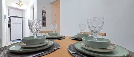 Une table à manger dressée avec de la vaisselle et des verres, un réfrigérateur et un élément décoratif suspendu au mur.