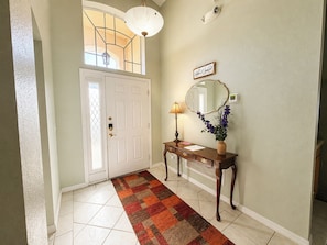 A hallway with a white door, a wooden console table with a lamp, a mirror, and a vase with flowers. - Beautiful Pool Home With Spa Overlooking Golf Course (Davenport)